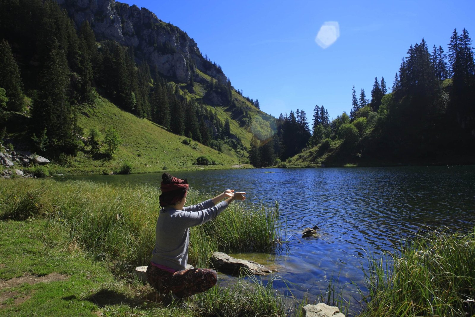 Sao Aum priant près d'un lac, avec une montagne verdoyante et des arbres en arrière-plan.