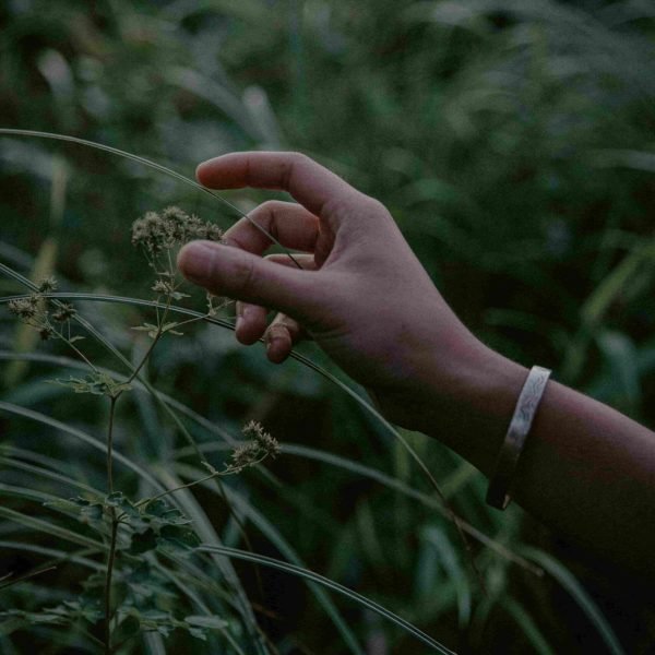 La main de Sao Aum avec un bracelet qui touche l'herbe, le soir.